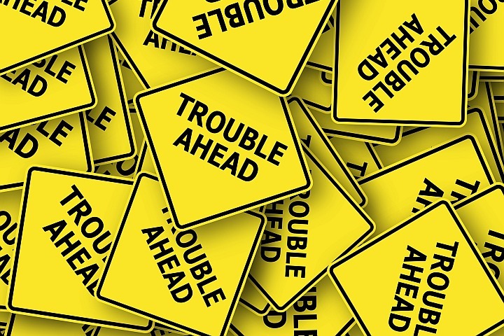 yellow road signs with black lettering that say "trouble ahead"
