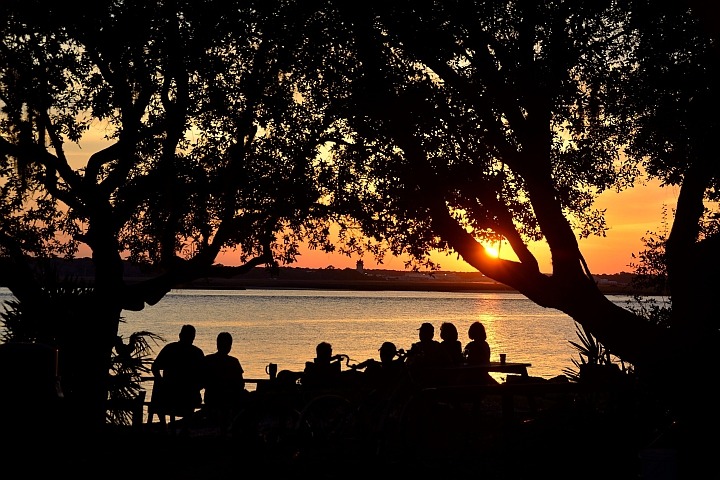 older people sitting on park bench looking at a sunset over the water
